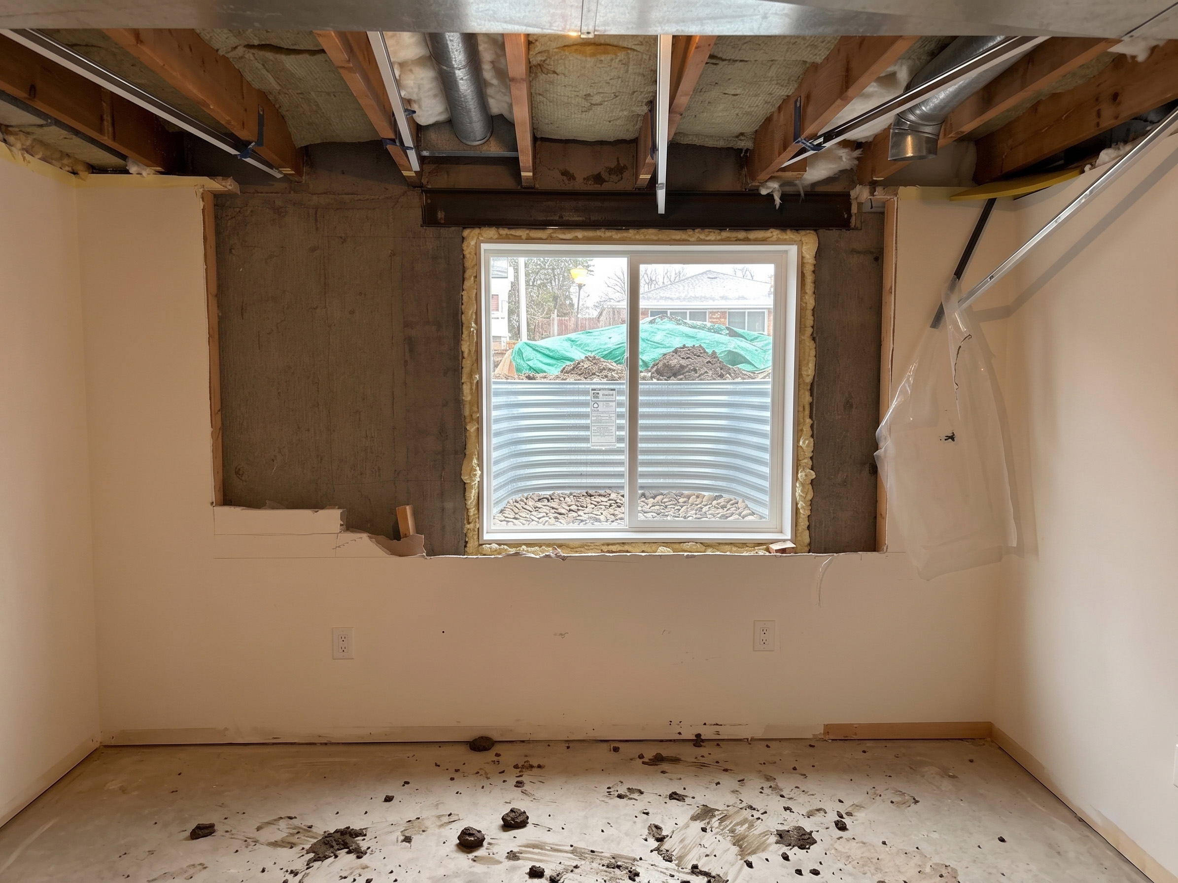 Unfinished basement with exposed framing, bare concrete, and dirt left behind around the egress window
