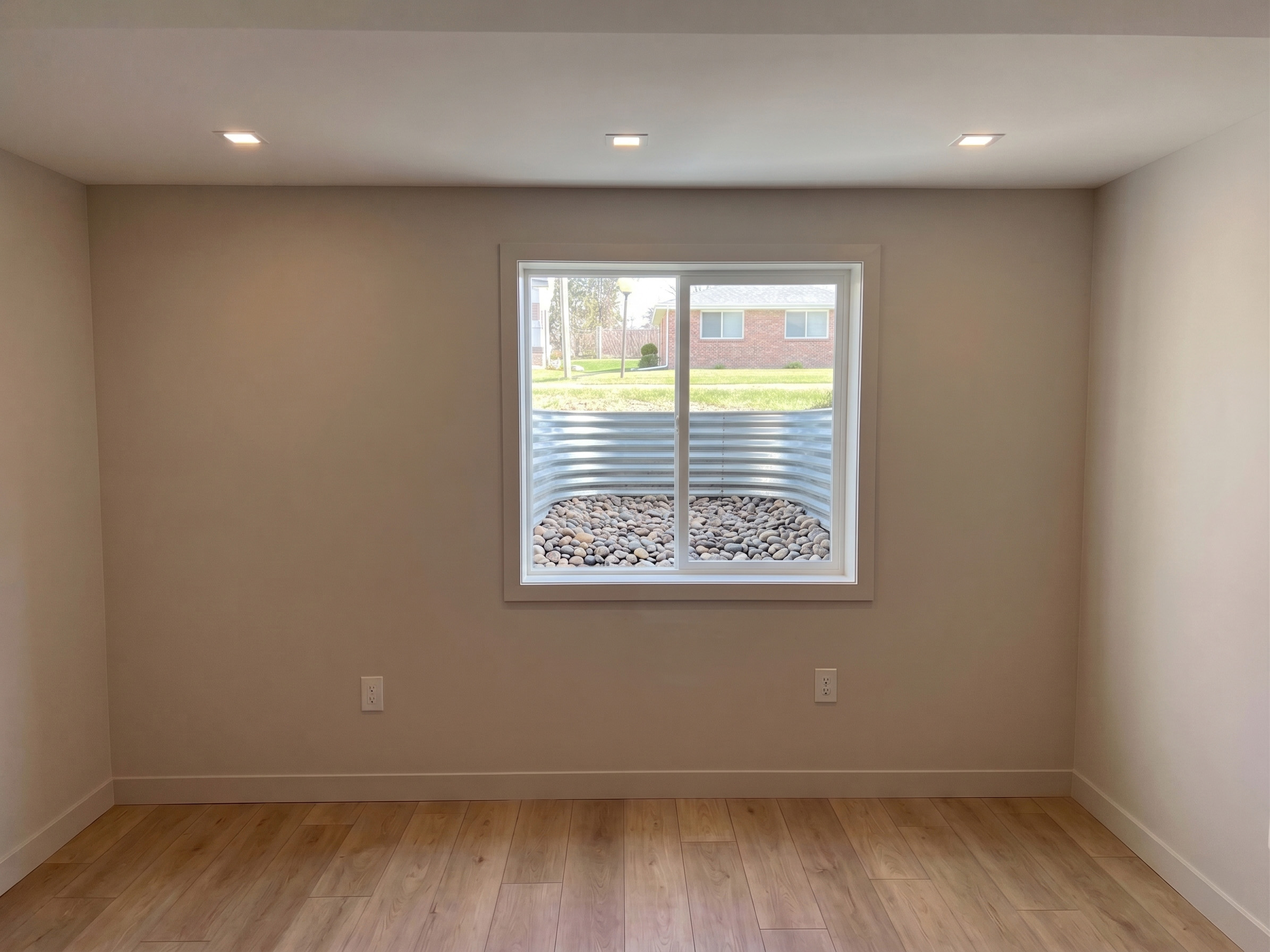 Fully finished basement bedroom with a clean egress window, painted walls, and flooring